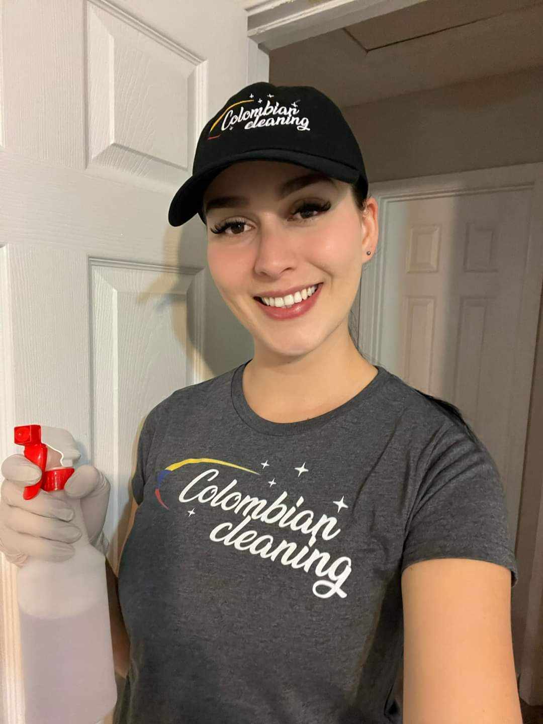 Smiling Colombian Cleaning employee wearing a branded t-shirt and cap, holding a spray bottle, ready for professional cleaning services.